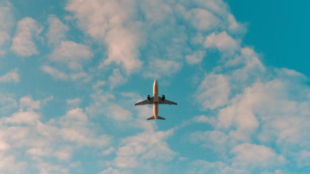 Ein Flugzeug fliegt vor blauem Himmel mit Wolken.