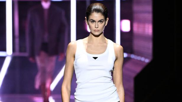 Kaia Gerber läuft in einem weißen Tanktop und einem Rock mit gelben Akzenten über einen Laufsteg.