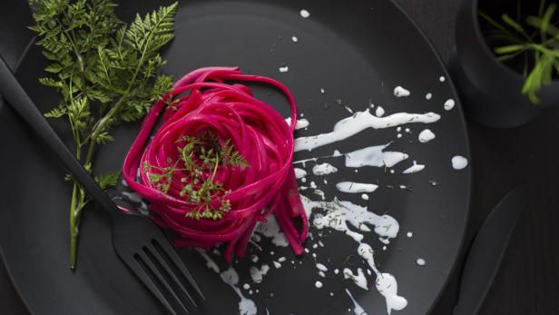 Ein Teller mit roter Pasta, garniert mit Dill und einer weißen Soße.
