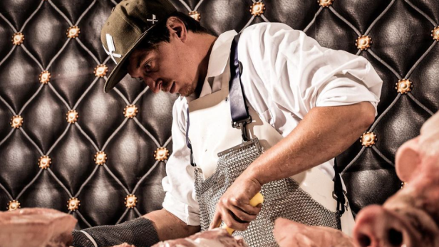 Ein Metzger mit Schürze und Kappe zerlegt Fleisch.