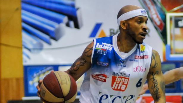 Ein Basketballspieler mit Tattoos und Stirnband hält einen Basketball.