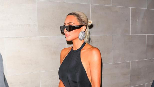 Kim Kardashian trägt einen schwarzen Overall, übergroße Ohrringe und eine „Balenciaga“-Sonnenbrille.