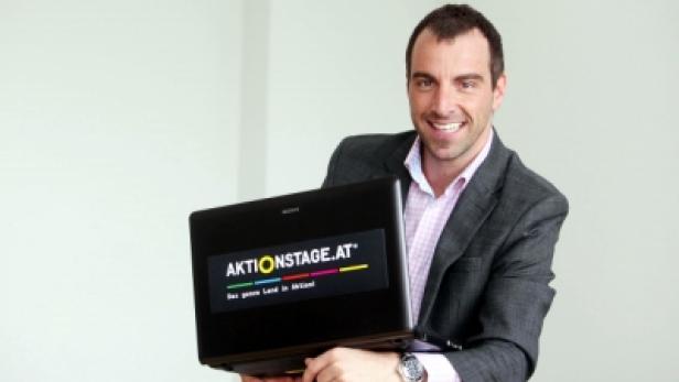 Ein Mann im Anzug hält einen Laptop mit dem Logo von aktionstage.at.
