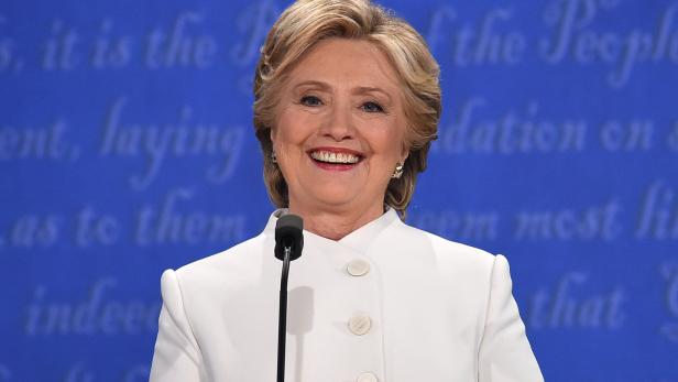 Hillary Clinton lächelt vor einem blauen Hintergrund am Rednerpult.