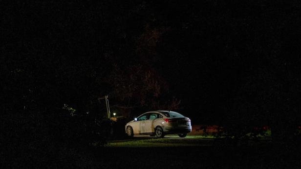 Ein weißes Auto steht nachts unter einer Straßenlaterne.