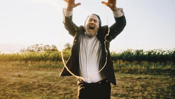 Ein Mann im Anzug steht auf einem Feld und wird mit Flüssigkeit übergossen.