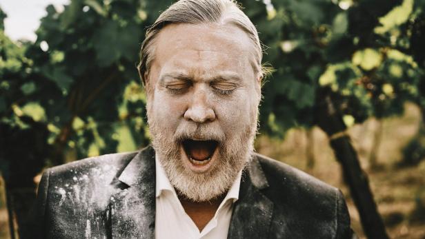 Ein Mann mit Bart und Anzug, bedeckt mit Puder, schreit vor einem Weinstock.
