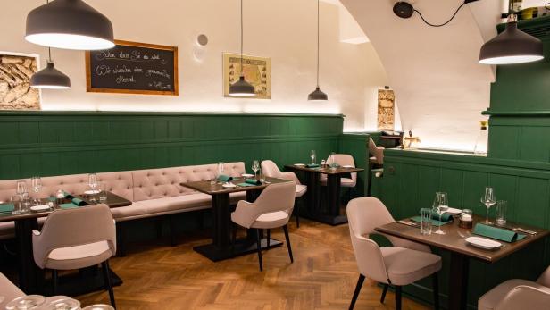 Einladender Gastraum mit gedeckten Tischen und grüner Wandvertäfelung.