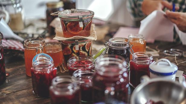 Verschiedene Gläser mit selbstgemachter Marmelade und eingelegten Feigen auf einem Holztisch.
