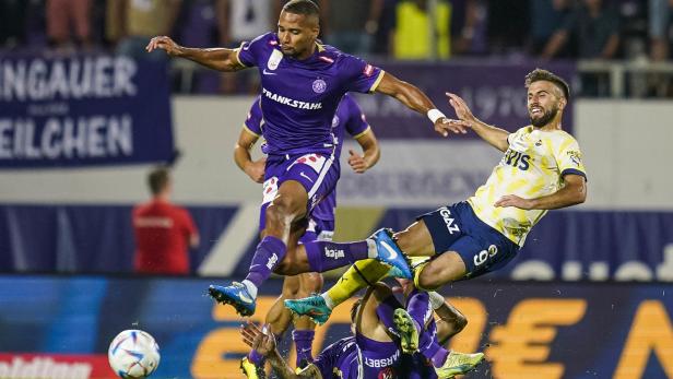 Ein Fußballspieler springt über zwei am Boden liegende Spieler während eines Fußballspiels.