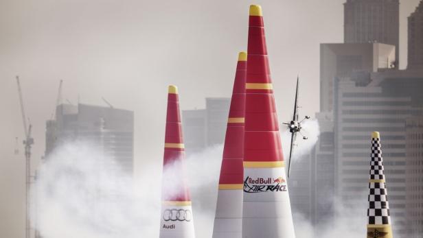 Ein Flugzeug fliegt bei einem Red Bull Air Race zwischen rot-gelben Pylonen hindurch.