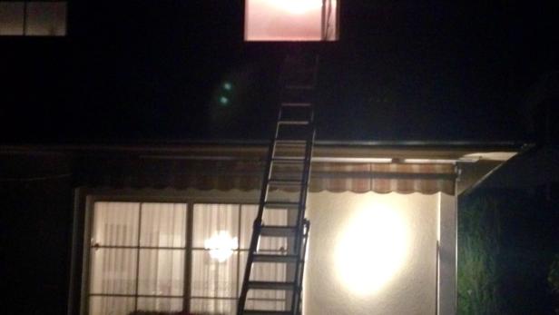 Eine Leiter lehnt nachts an einem Haus, um eine Lampe zu erreichen.