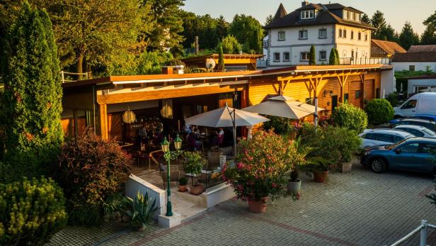 Ein Restaurant mit Gästen im Außenbereich und einem Parkplatz im Hintergrund.