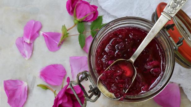 Ein Glas und ein kleiner Löffel mit Teerosenblütenmarmelade auf hellem Marmorhintergrund.