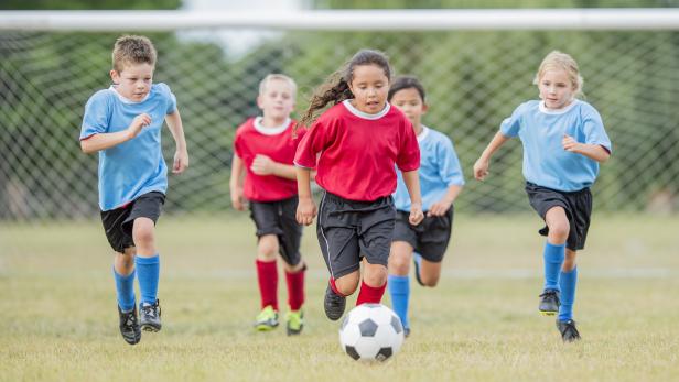 Fünf Kinder spielen Fußball auf einem Rasenplatz und rennen zum Ball.