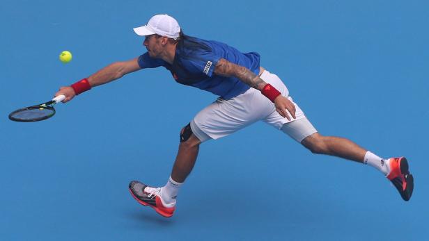 Ein Tennisspieler schlägt einen Ball vor einem blauen Hintergrund.