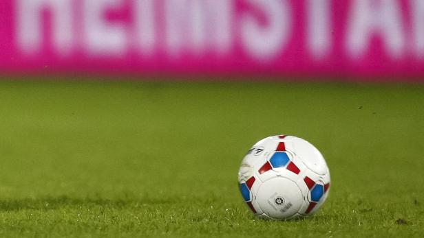 Ein Fußball liegt auf einem grünen Rasen vor einer pinkfarbenen Werbetafel.