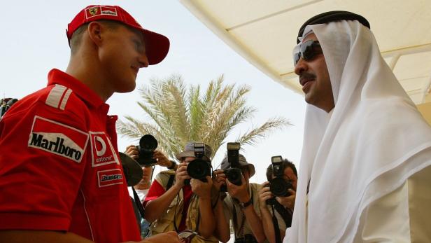 Michael Schumacher trifft einen Mann in traditioneller arabischer Kleidung vor einer Gruppe von Fotografen.