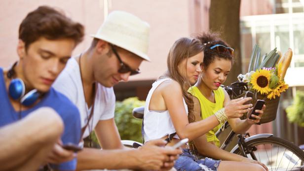 Eine Gruppe junger Leute sitzt im Freien und benutzt ihre Smartphones.