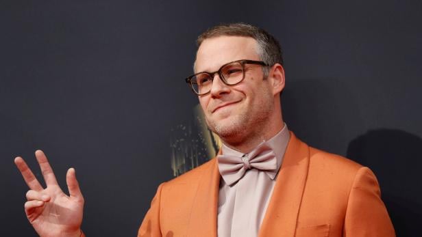 Seth Rogen in einem orangefarbenen Anzug mit Fliege gestikuliert.