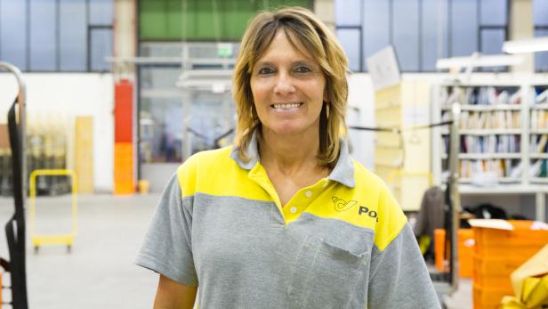 Eine freundliche Postangestellte in ihrer Arbeitskleidung lächelt in die Kamera.