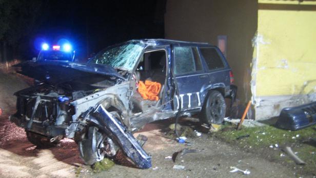 Ein schwer beschädigter blauer Jeep nach einem Unfall, mit Blaulicht im Hintergrund.