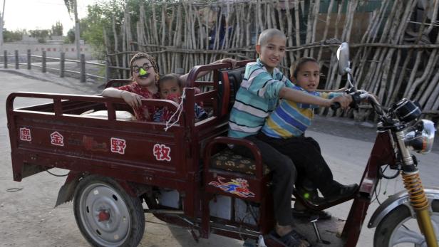 Mehrere Kinder fahren mit einem motorisierten Dreirad auf einer Straße.