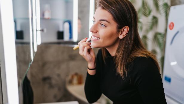 Eine Frau trägt Make-up vor einem Spiegel im Badezimmer auf.