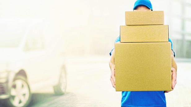 delivery man holding pile of cardboard boxes in front