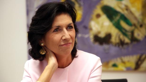 Eine Frau mit dunklen Haaren und rosa Jacke blickt nach rechts.