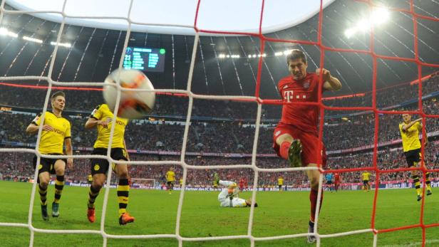 Ein Fußballspieler schießt den Ball ins Tor, während andere Spieler zusehen.