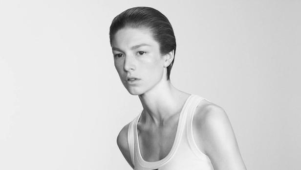 Eine Frau mit kurzem, dunklem Haar trägt ein weißes Tanktop von Prada und einen schwarzen Rock.