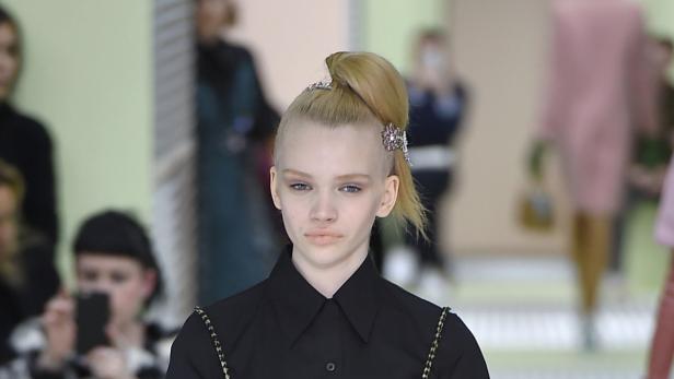 Ein Model mit hochgesteckten blonden Haaren und Haarspangen auf einem Laufsteg.