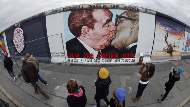 Tourists look at the mural by Russian artist Dmitry Vrubel of former Soviet leader Leonid Brezhnev kissing his East German counterpart Erich Honecker, painted on a segment of East Side Gallery, the largest remaining part of the former Berlin Wall, in Berlin October 30, 2009. A 1,300 metres (4,265 ft) stretch of wall, the world&#039;s longest open-air art gallery, was decorated by 118 artists from 21 countries in 1990, but has since been damaged by the weather, exhaust fumes, vandals, and souvenir-seeking tourists. The restoration work is expected to be completed in time for the 20-year anniversary in November of the fall of the wall which once divided communist East Berlin from capitalist west Berlin. REUTERS/Fabrizio Bensch (GERMANY ENTERTAINMENT SOCIETY POLITICS ANNIVERSARY)
