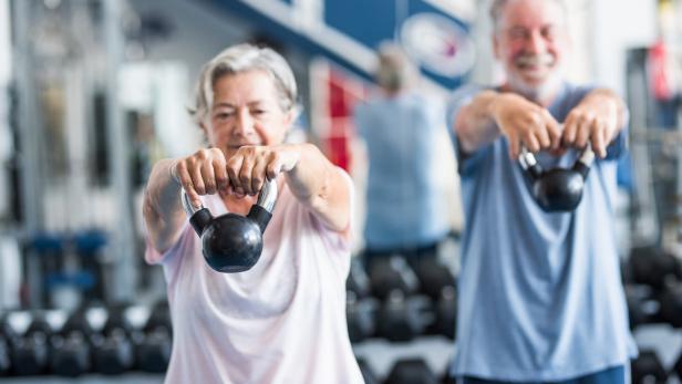 Ein älteres Paar hebt Kettlebells hoch.