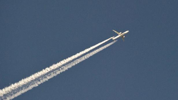 Ein Flugzeug zieht Kondensstreifen am blauen Himmel entlang.