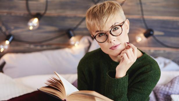 Eine Frau mit Brille liest ein Buch im Bett.