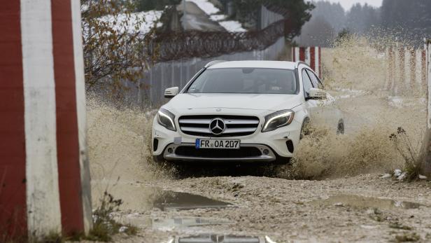Ein weißer Mercedes-Benz fährt durch eine schlammige Wasserfläche.