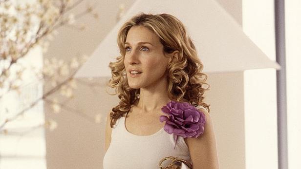 Sarah Jessica Parker, mit lila Blume, Handtasche und Jacke, in einer Szene aus „Sex and the City“.