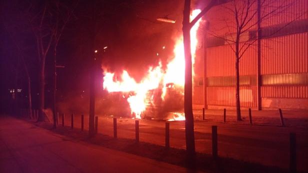 Ein brennendes Fahrzeug steht nachts vor einem Gebäude.