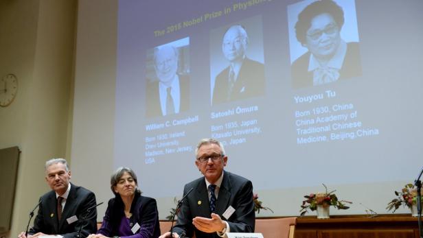Drei Personen sitzen vor einer Leinwand mit den Porträts der Nobelpreisträger von 2015.