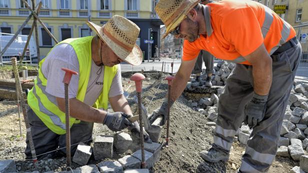 Zwei Bauarbeiter verlegen Pflastersteine auf einer Baustelle.