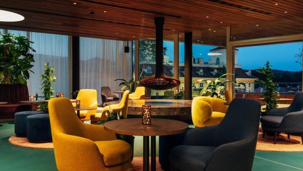 Ein modern gestalteter Loungebereich mit Sesseln, Tischen und einem hängenden Kamin.