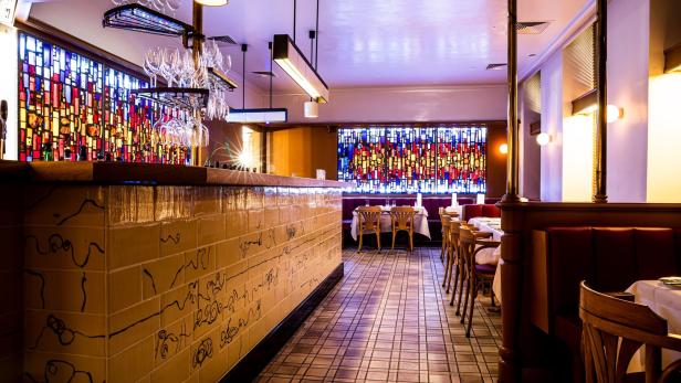 Innenansicht eines eleganten Restaurants mit Buntglasfenstern und gedeckten Tischen.