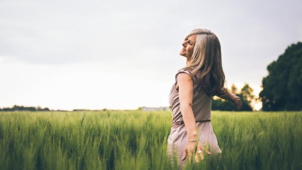 Eine Frau steht mit offenen Armen in einem grünen Feld.