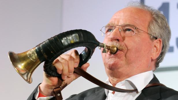 Ein Mann mit Brille und Schnurrbart bläst in ein Jagdhorn.