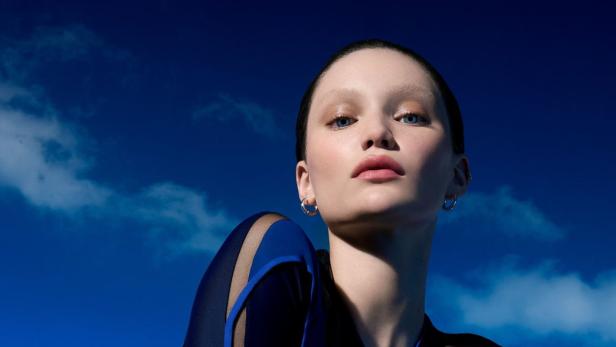 Eine Frau mit blauem Kleid posiert vor einem blauen Himmel.