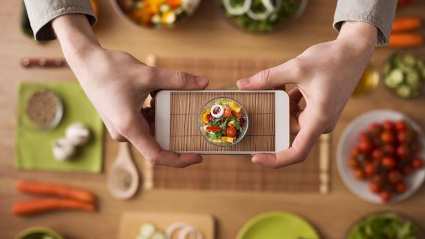 Jemand fotografiert einen bunten Salat mit einem Smartphone.