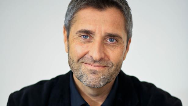 Porträt eines lächelnden Mannes mit grauen Haaren und blauen Augen.