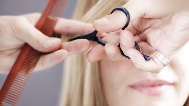 Ein Friseur schneidet einer blonden Frau die Haare.